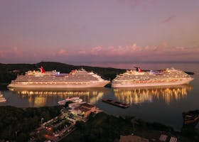Two illuminated cruise ships docked at Coxen Hole, Honduras during twilight.